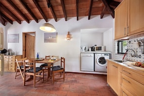 A kitchen with wooden cabinets, a washing machine, and a dining area with a table and chairs.