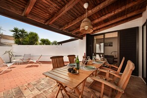 An outdoor patio with a wooden table set for dining, surrounded by wooden chairs.