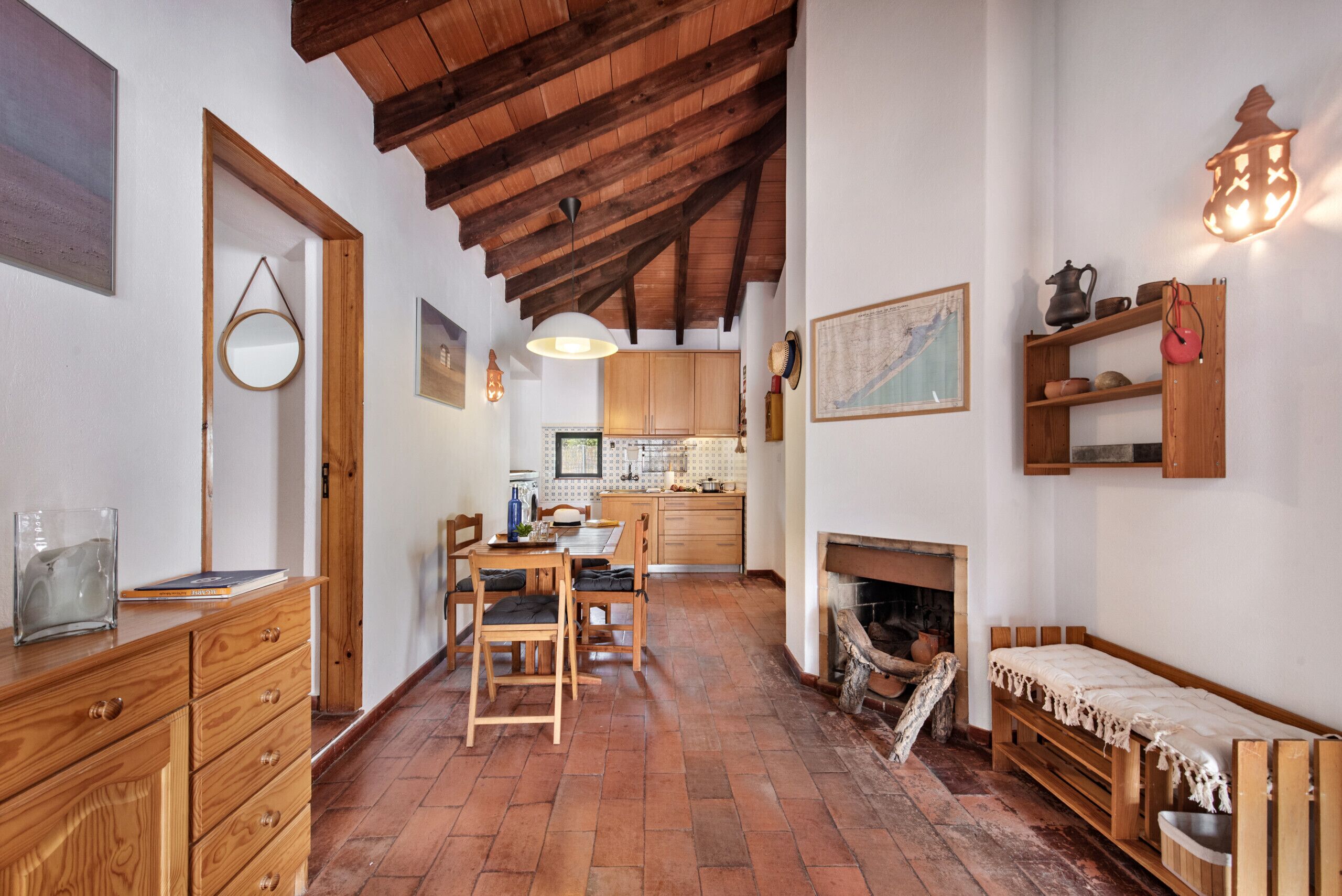 A rustic interior with a wooden dining table, chairs, a fireplace, and a kitchen in the background.