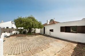 Une cour avec un patio dallé, un arbre et un bâtiment blanc doté d’un toit en tuiles.