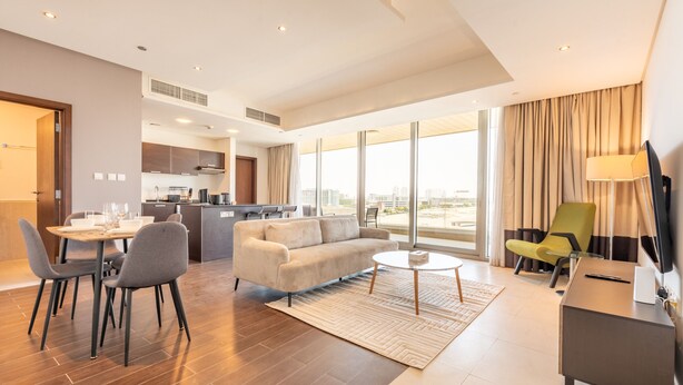 Habitación de hotel moderna con zona de comedor, sofá, televisión y vistas a la ciudad.