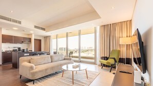 Habitación de hotel moderna con sofá, mesa de centro, televisor y vista de la ciudad a través de amplias ventanas.
