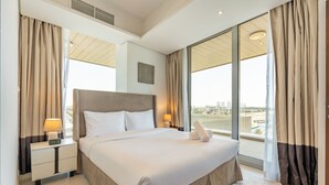 Habitación de hotel moderna con una cama grande, una mesita de noche con lámpara y vistas de la ciudad a través de amplios ventanales.