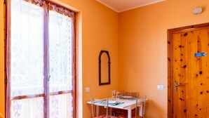 A dining area with a table set for four, a wooden door with a 'No Smoking' sign, and a window with sheer curtains. - Casa Anna by Interhome (Pompeiana)