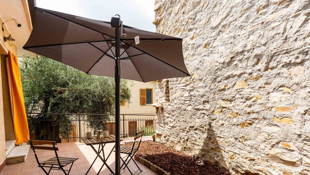 A patio with a table and chairs, a large umbrella, and a stone wall. - Casa Anna by Interhome (Pompeiana)
