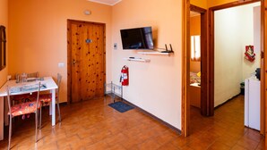 A room with a wooden door, a television mounted on the wall, a small table with chairs, and a fire extinguisher. - Casa Anna by Interhome (Pompeiana)