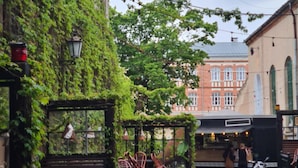 A cobblestone street with a covered outdoor seating area, wicker chairs, and a building with a brick facade in the background.