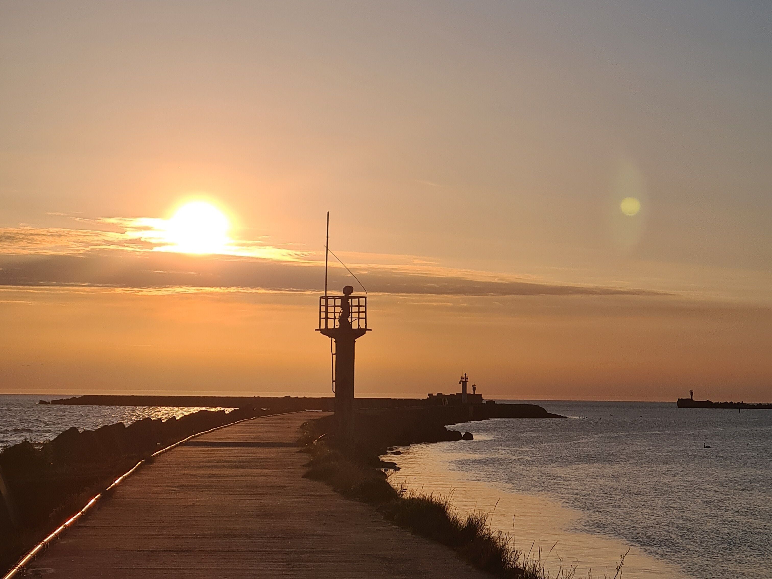 A wooden pier extending into calm waters with a lighthouse in the distance.