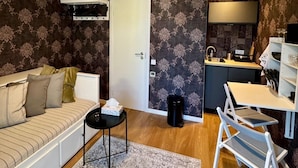 A compact living space with a sofa, a small table, a kitchen area with a sink and cabinets, and a door leading to another room.