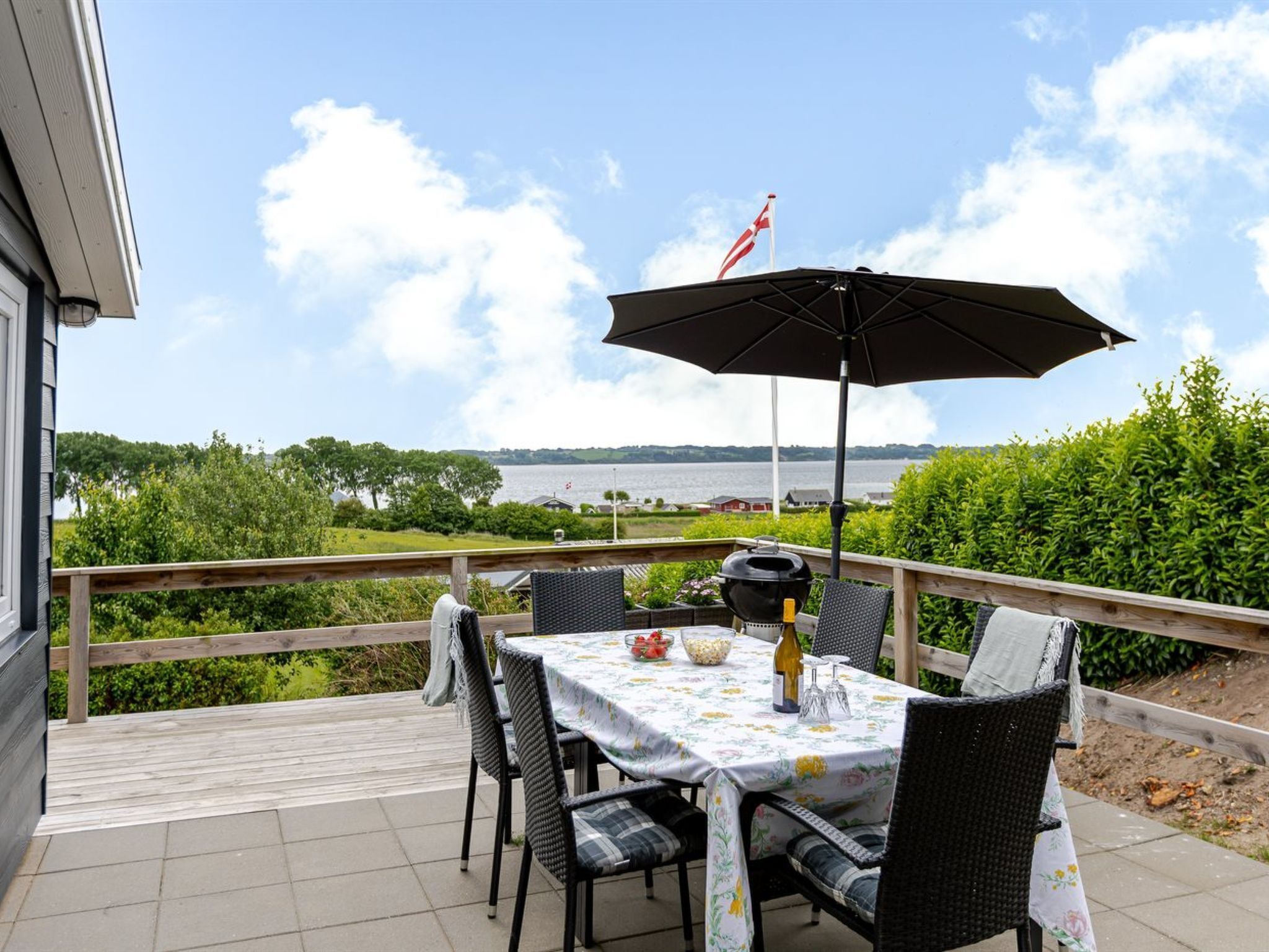 Een terras buiten met een tafel voor twee personen, een barbecue en uitzicht op een waterpartij.