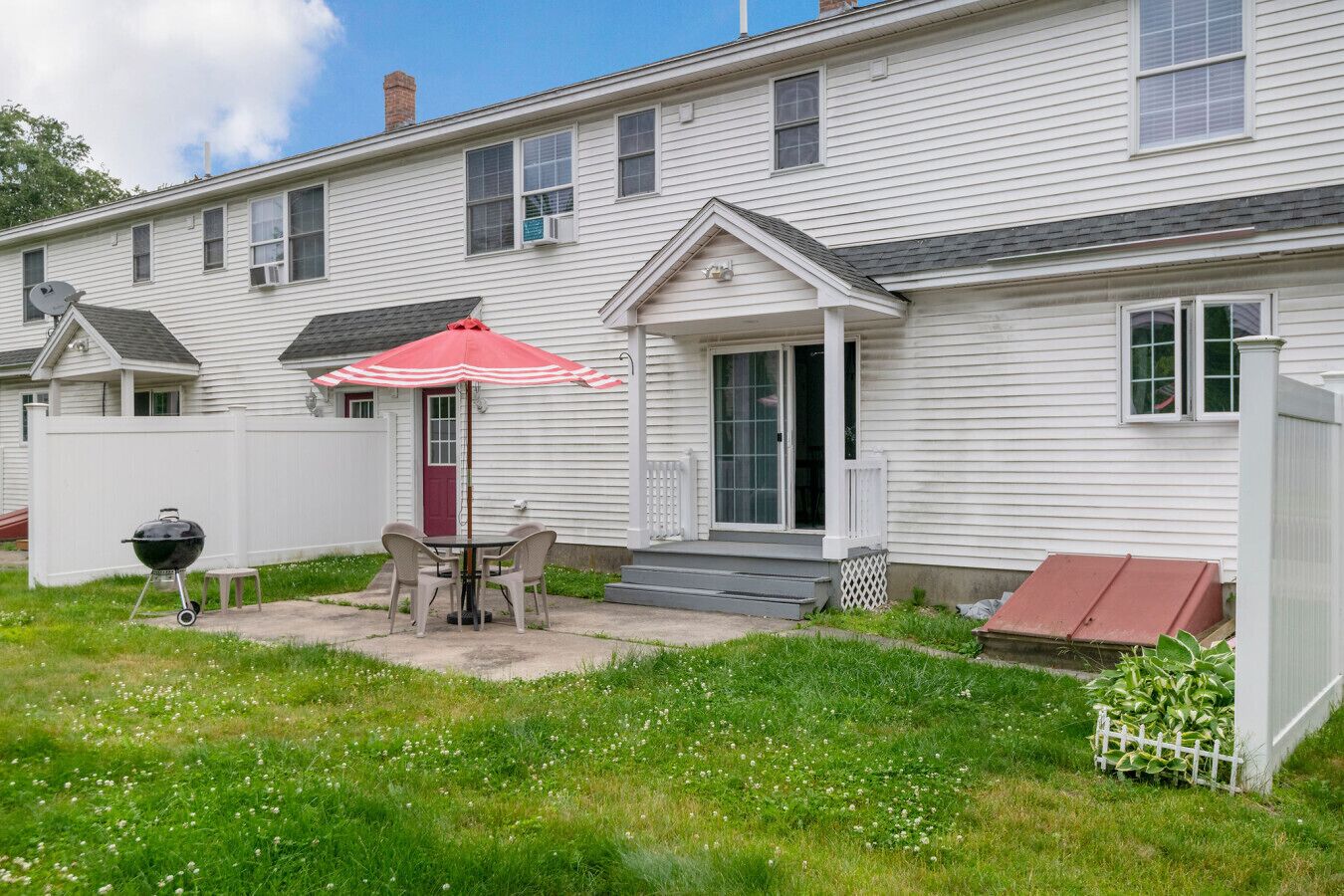 A white house with a patio, a grill, and a red umbrella.
