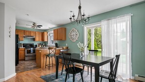 A modern kitchen with wooden cabinets, a central island, and a dining area with a black table and chairs.