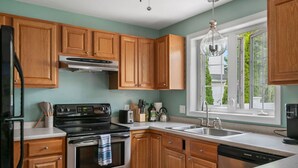 A kitchen with wooden cabinets, a stainless steel stove, a dishwasher, and a window with a view of greenery.