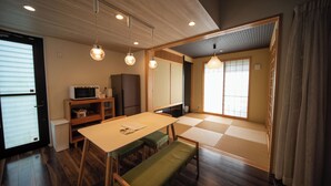 Una habitación japonesa tradicional con suelo de tatami, una mesa baja con bancos, un microondas y puertas correderas.