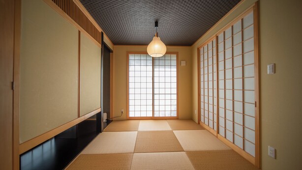 Una habitación japonesa tradicional con suelo de tatami, puertas correderas y una lámpara colgante.