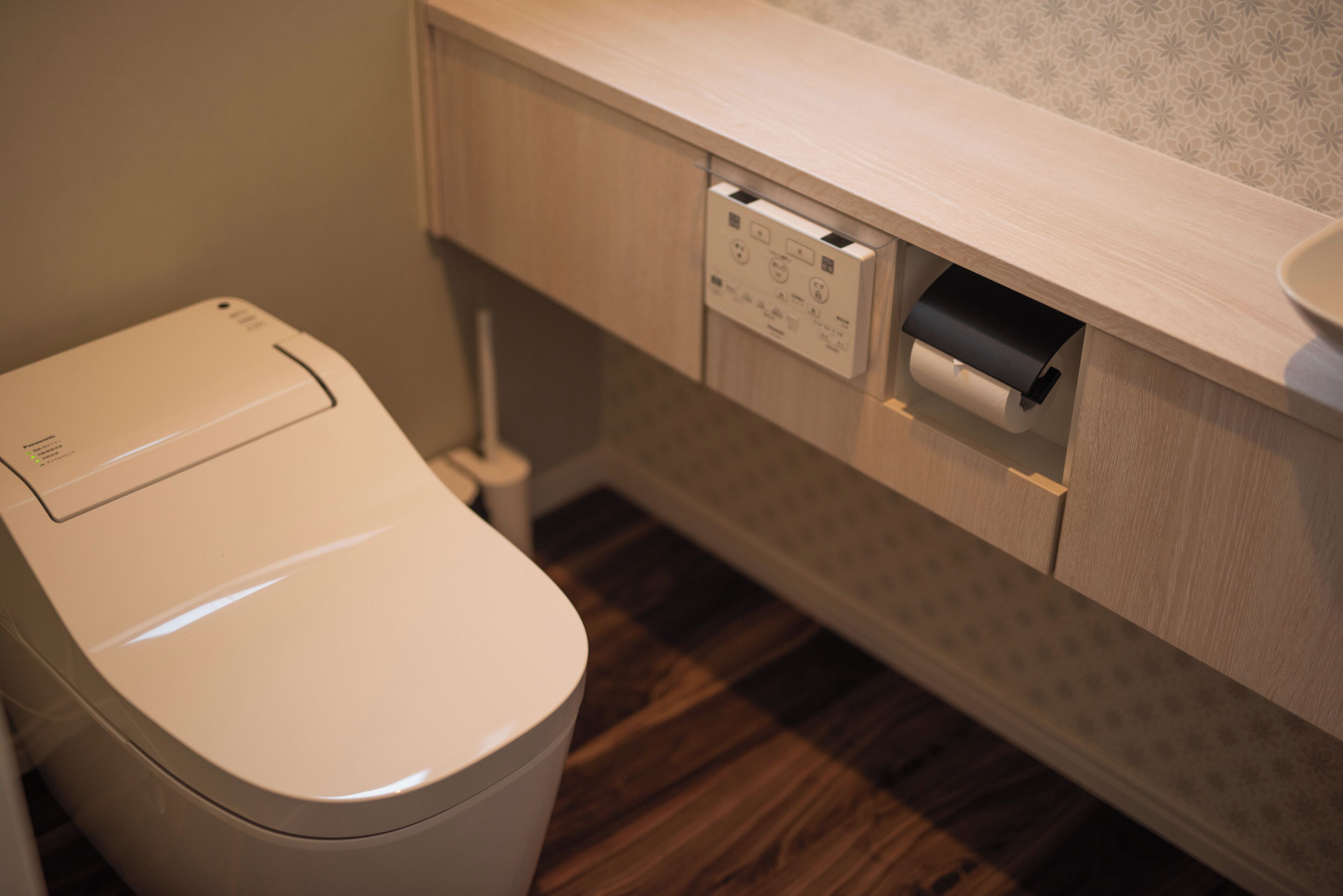 A modern bathroom with a toilet, a paper towel dispenser, and a wooden floor.
