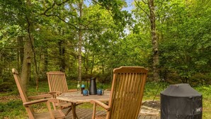 Une terrasse en bois avec une table et des chaises, entourée d’une forêt.