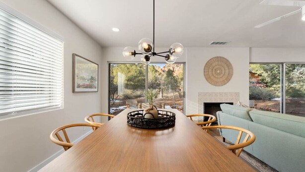 Un comedor con mesa de madera, sillas, una lámpara de araña y vistas al exterior a través de amplios ventanales.