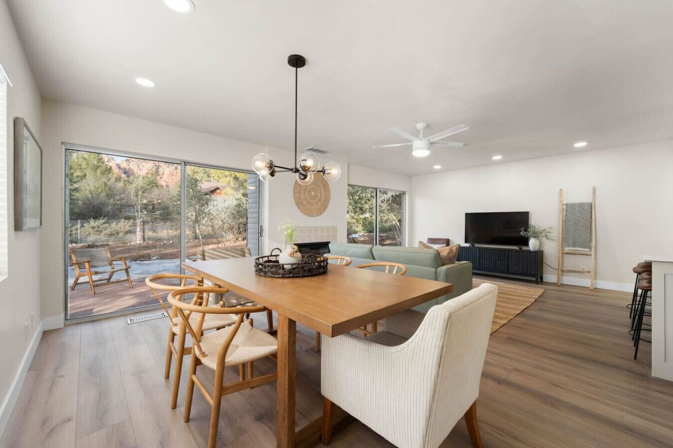 Amplia sala de estar con una mesa de comedor de madera, asientos cómodos, un televisor grande y vistas al exterior.