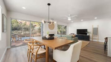 Amplia sala de estar con una mesa de comedor de madera, asientos cómodos, un televisor grande y vistas al exterior.