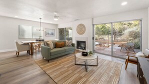 Una sala de estar moderna con sofá, mesa de centro y chimenea, que da a un patio con mobiliario exterior.
