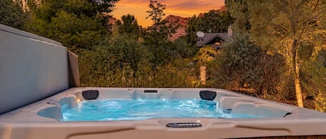 Un jacuzzi en un recinto de madera con vistas a árboles y una casa al fondo.