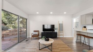 Una sala de estar moderna con un televisor grande, una silla de madera y una zona de comedor con taburetes de bar.