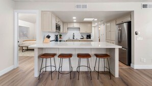 Una cocina moderna con una isla central, taburetes de bar, electrodomésticos de acero inoxidable y armarios de tonos claros.