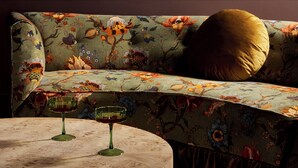 Un sofá con tapicería floral, una mesa redonda de mármol con dos vasos, y un cojín dorado.