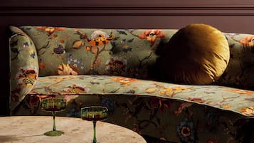A sofa with floral upholstery, a round marble table with two glasses, and a gold pillow.