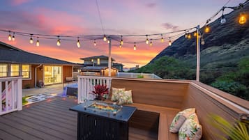 A deck with a fire feature, seating, and string lights against a sunset backdrop.