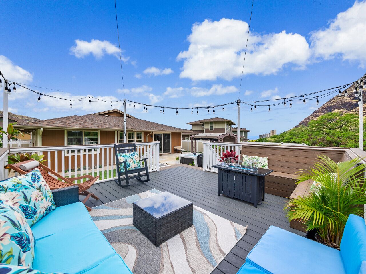 A covered outdoor patio with seating, string lights, and a view of a hillside.