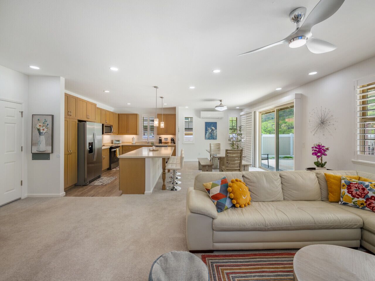 Una cocina moderna con una isla central, un comedor con mesa y sillas, y una sala de estar con sofá y cojines decorativos.