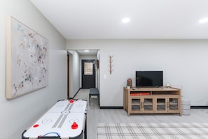 Une pièce avec une table de baby-foot, un téléviseur posé sur un meuble en bois, et un couloir menant à une autre pièce.