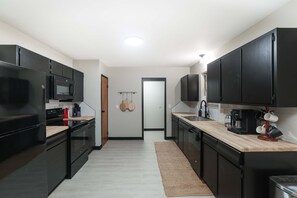 Une cuisine moderne avec des meubles de couleur noire, un four à micro-ondes, une machine à café et un plan de travail en bois.