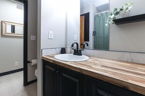 A bathroom with a wooden vanity, a white sink, a black faucet, a mirror, and a potted plant. - Dazzling East Side 3BR 2 BA Coffee/WFI/SMRT TV (Wichita)
