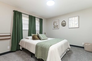 A bedroom with a bed, green curtains, a bedside table, a wall-mounted mirror, and two framed artworks. - Dazzling East Side 3BR 2 BA Coffee/WFI/SMRT TV (Wichita)