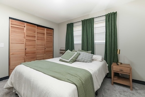Une chambre à coucher avec un lit, une table de chevet, une armoire en bois et des rideaux verts.
