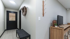 Un couloir avec une porte noire, un banc, un porte-manteau fixé au mur, une petite table avec une plante et un téléviseur.