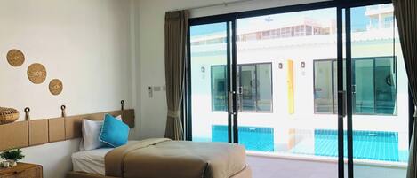 A hotel room with a bed, a bedside table, a window with curtains, and a view of a swimming pool.
