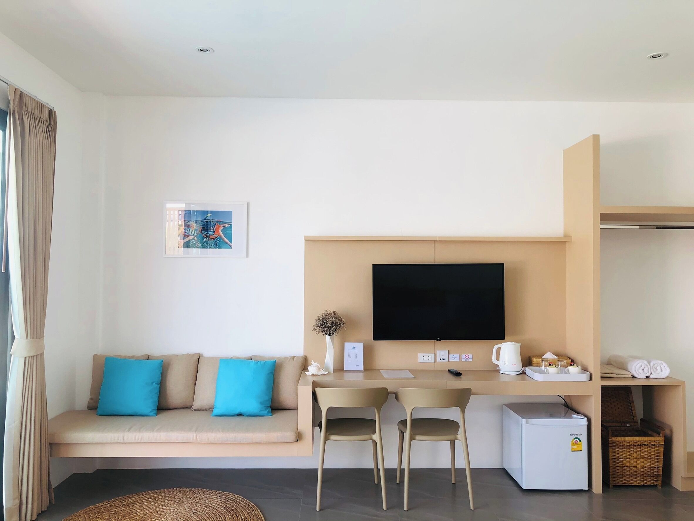 Ein modernes Hotelzimmer mit Sofa, Esstisch mit Stühlen, Flachbildfernseher, Kaffeemaschine und kleinem Kühlschrank.