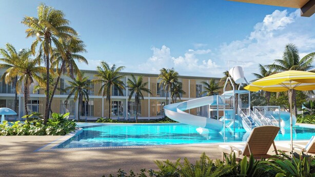A swimming pool with a water slide, palm trees, and a building with balconies in the background.