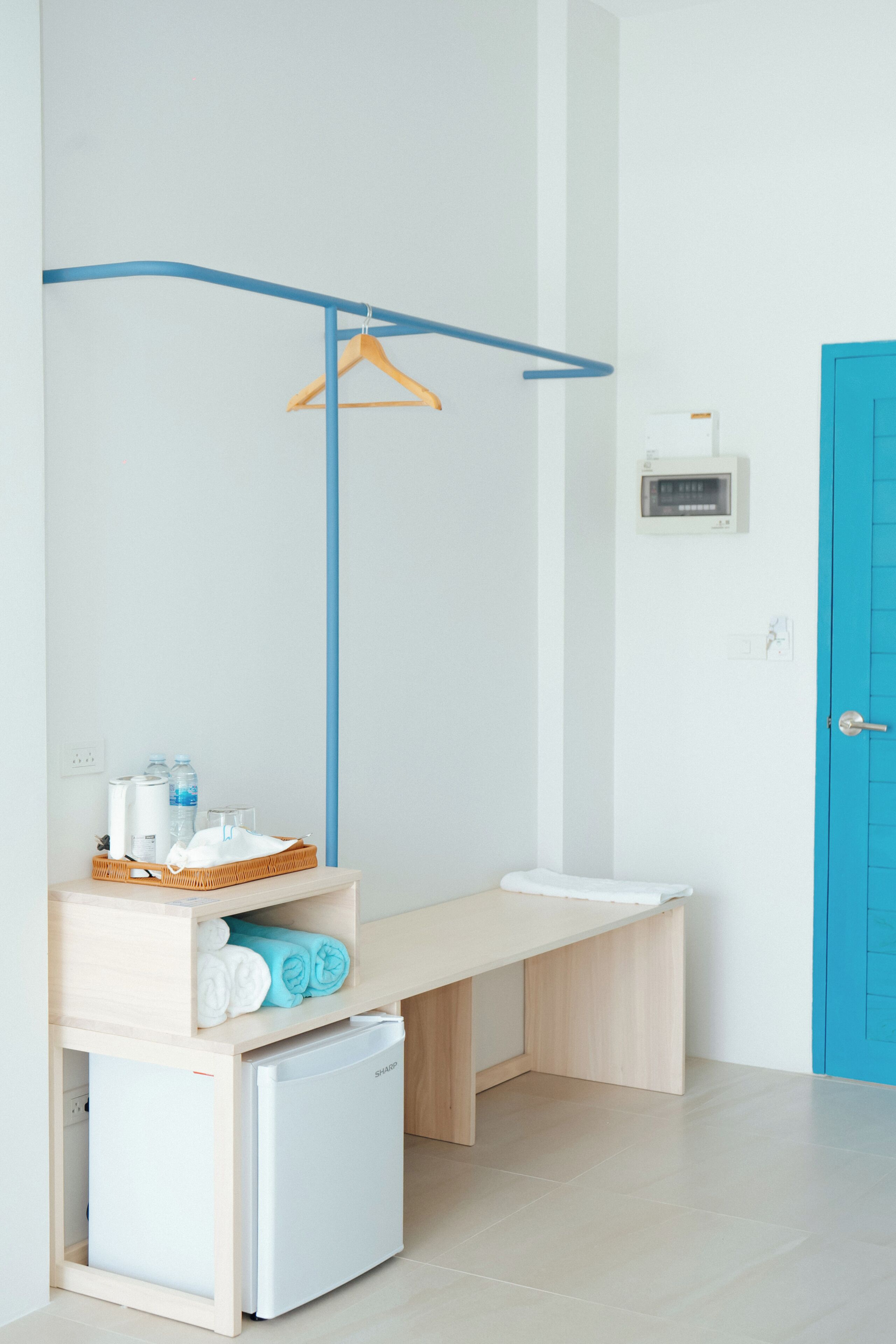 A modern bathroom with a white sink, a small white refrigerator, a blue door, and a towel rack.