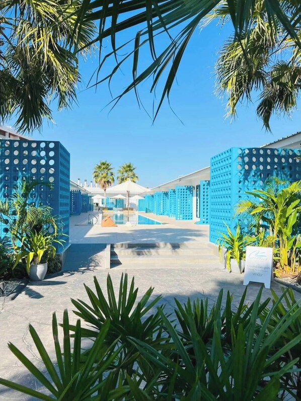 Een resort met een zwembadgedeelte, blauwe structurele elementen en tropische planten.