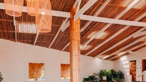 A spacious room with wooden benches and tables, bamboo ceiling beams, and hanging light fixtures.