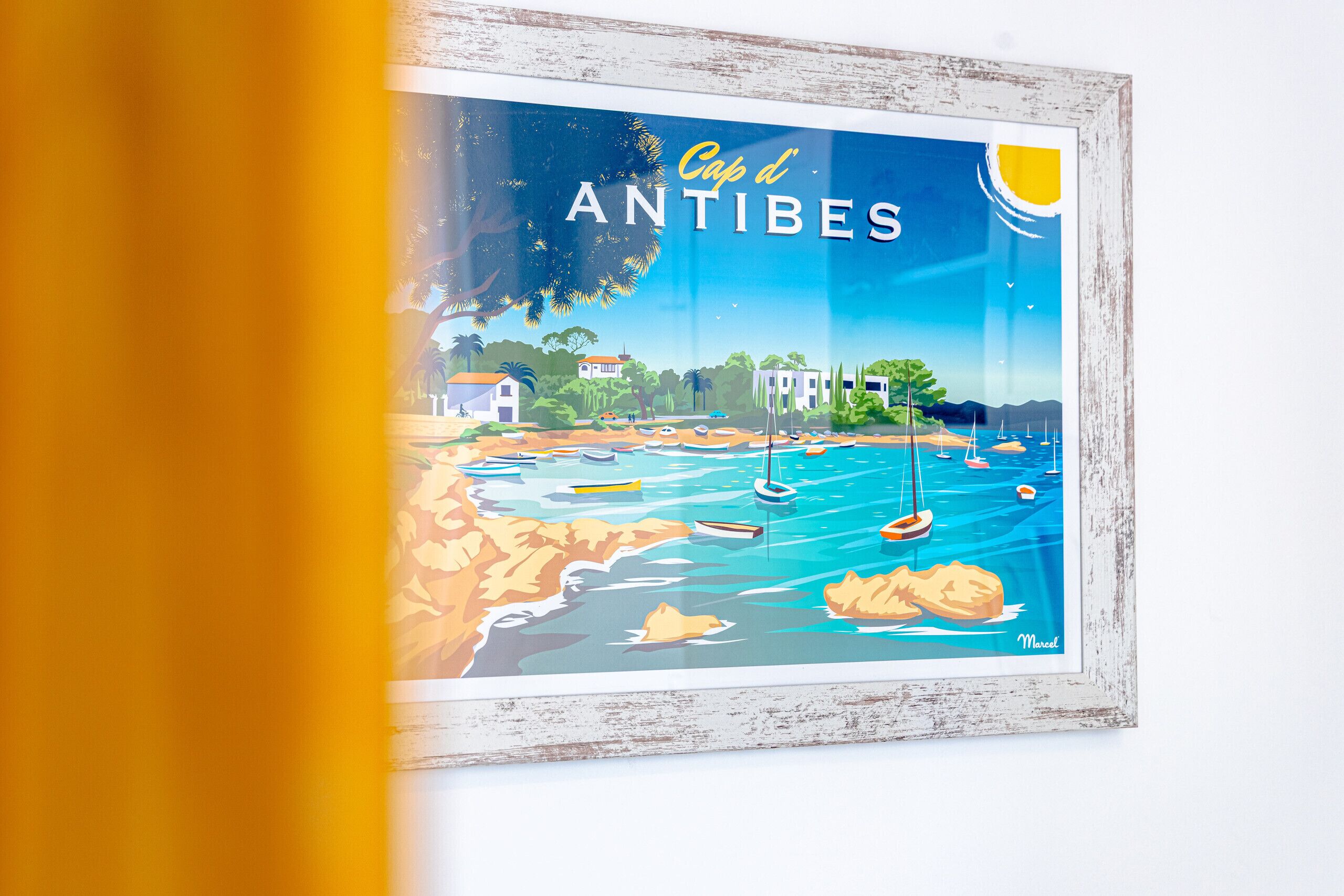 Una ilustración enmarco del Cap d'Antibes con una escena costera, que incluye barcos y edificios.