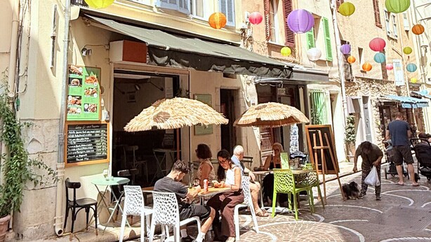 Una calle con mesas al aire libre, un edificio con muchas ventanas y faroles de papel de colores.
