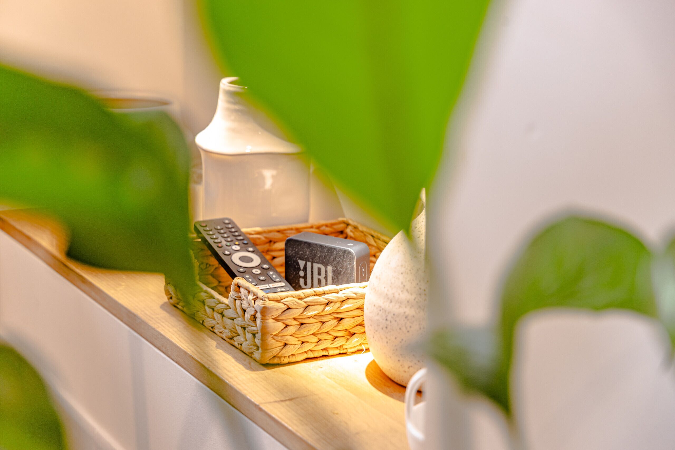 A wooden shelf with a woven basket containing a remote control, a small white container, and a decorative item.
