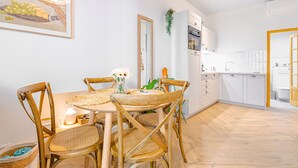 Una cocina moderna con armarios blancos, una mesa de comedor de madera con sillas y una planta colgante.