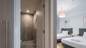 A modern hotel room with a shower area, a bed with white bedding, and a bedside table.